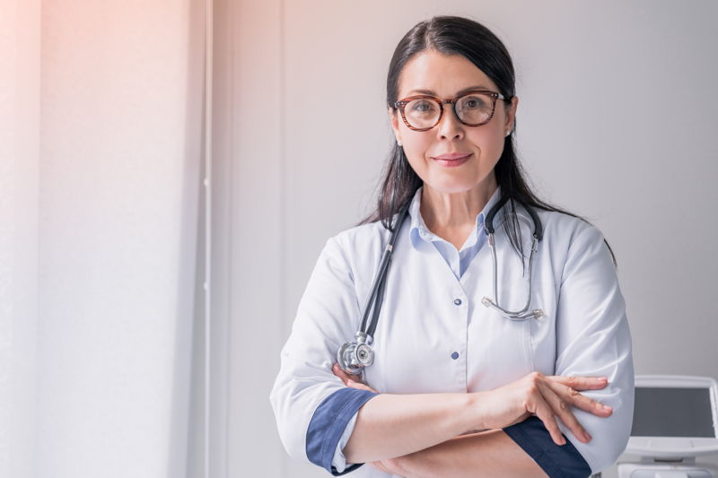 datenschutz arztpraxis Eine Ärztin mit dunklen Haar und Brille, die ein Stethoskop um den Hals trägt.